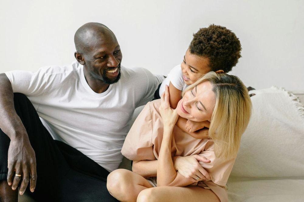 A father and mother laughing with their young child on a sofa