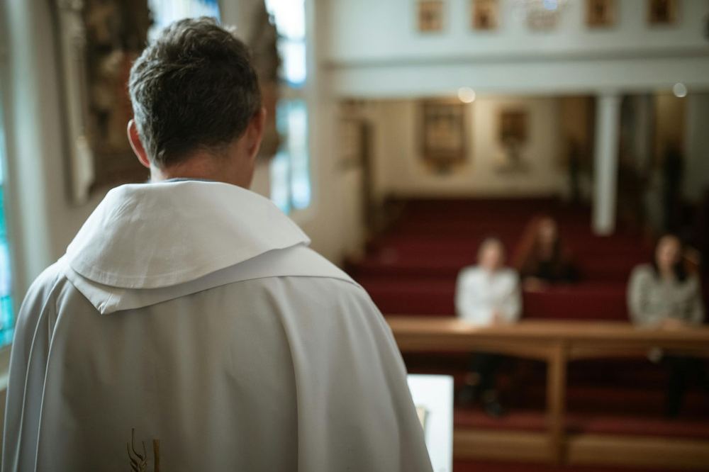 A minister in a white robe facing a small congregation