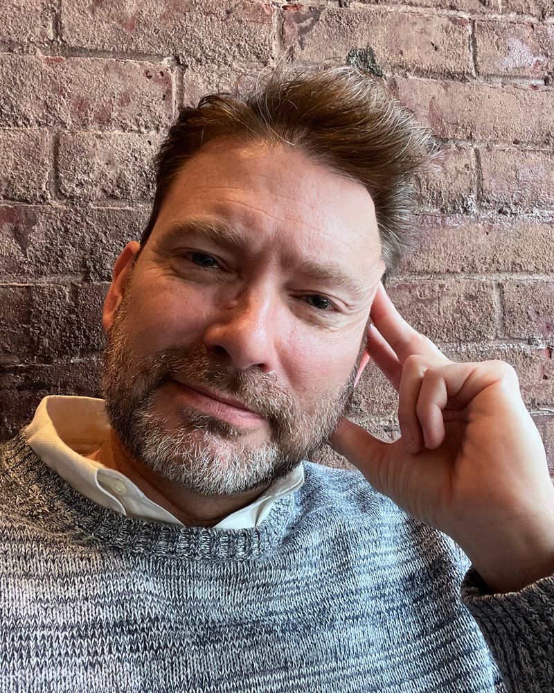 Michael Droege, smiling, seated against a brick wall