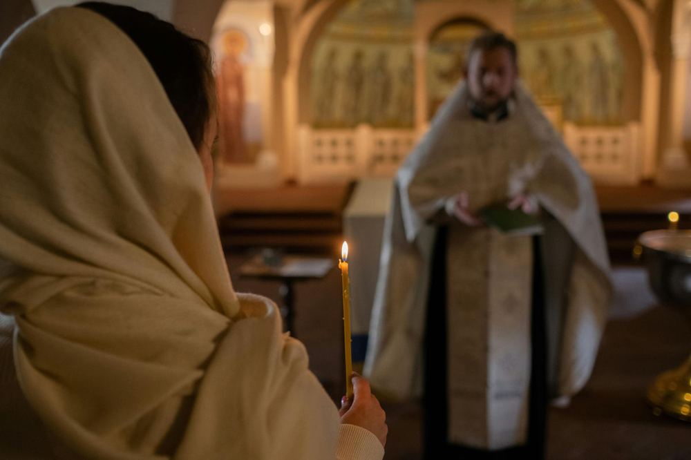 A worshipper and a priest in a candlelit sanctuary